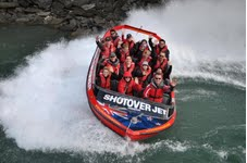 Shotover Jet passengers enjoy their ride in a Shotover Jet boat proudly bearing the New Zealand flag