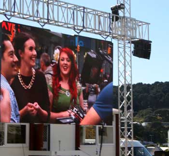 Johnson Witehira, left and Elspeth Hoskin (centre) are viewed on a big screen erected on the forecourt of Massey's Wellington campus as part of a live stream to New York's Times Square where their own artwork was showcased on digital billboards.  